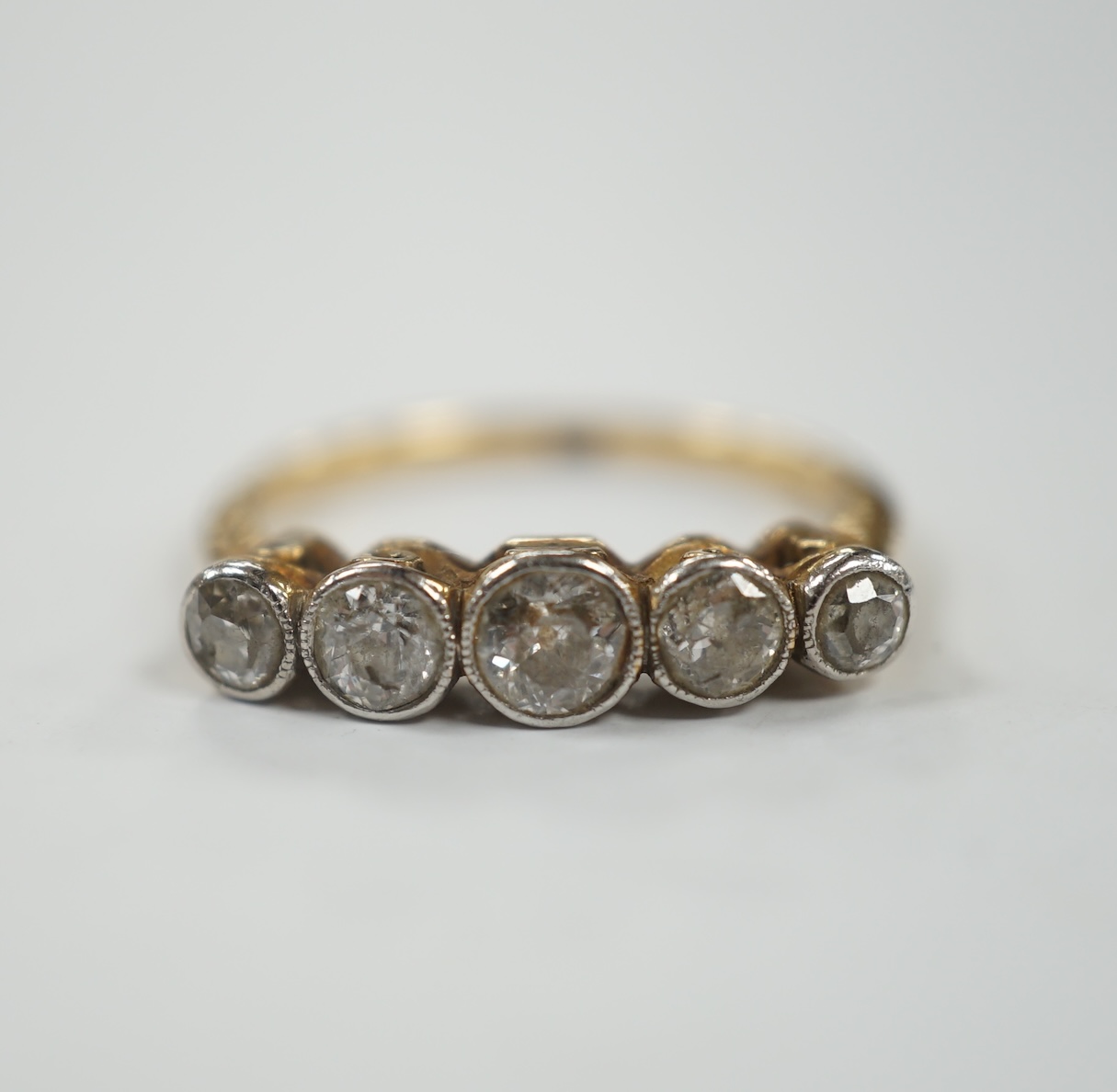 A yellow metal (stamped 18) and graduated five stone diamond set half hoop ring, size M/N, gross weight 3 grams.